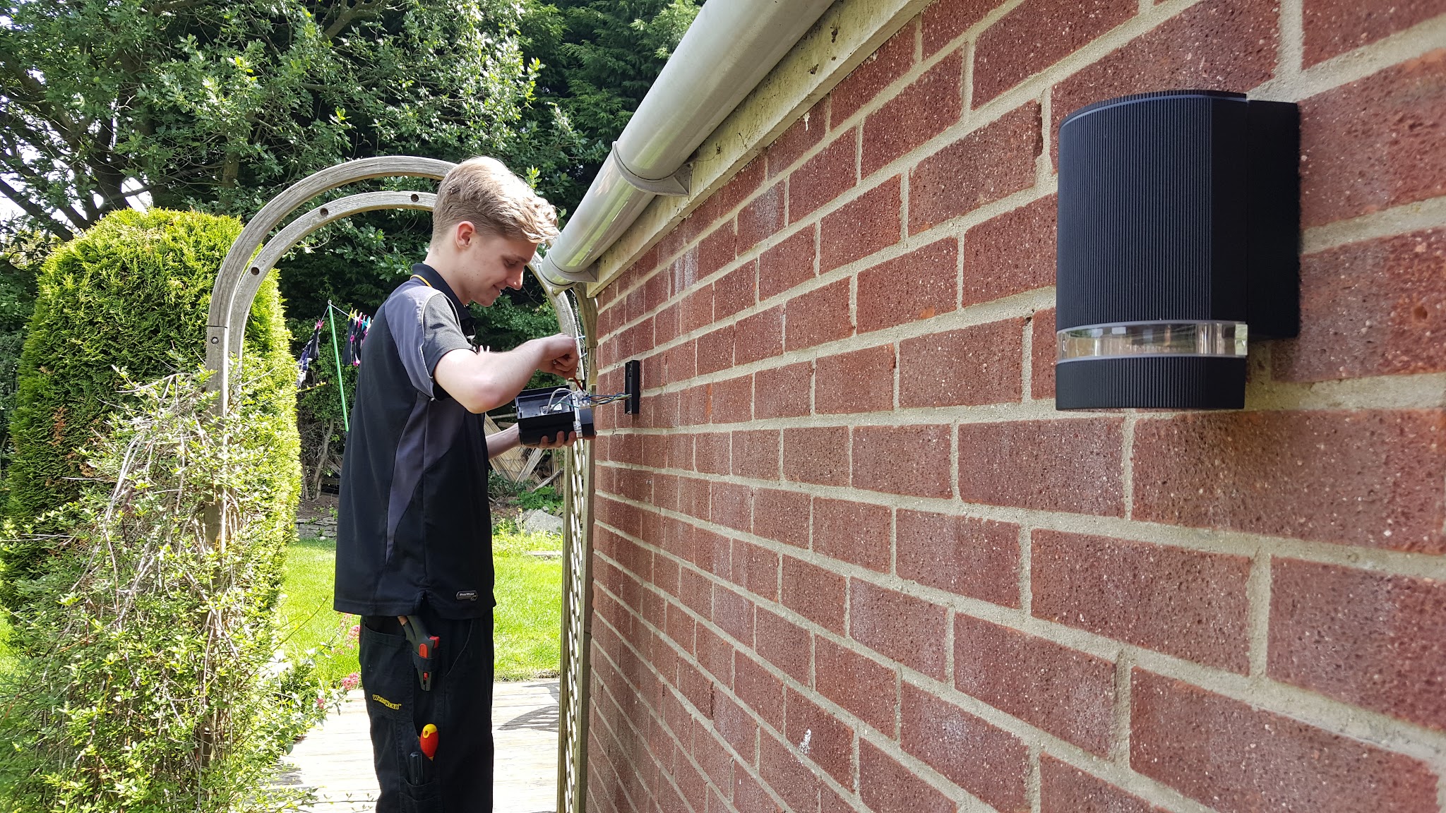 An electrician fitting an outdoor wall light on a brick wall