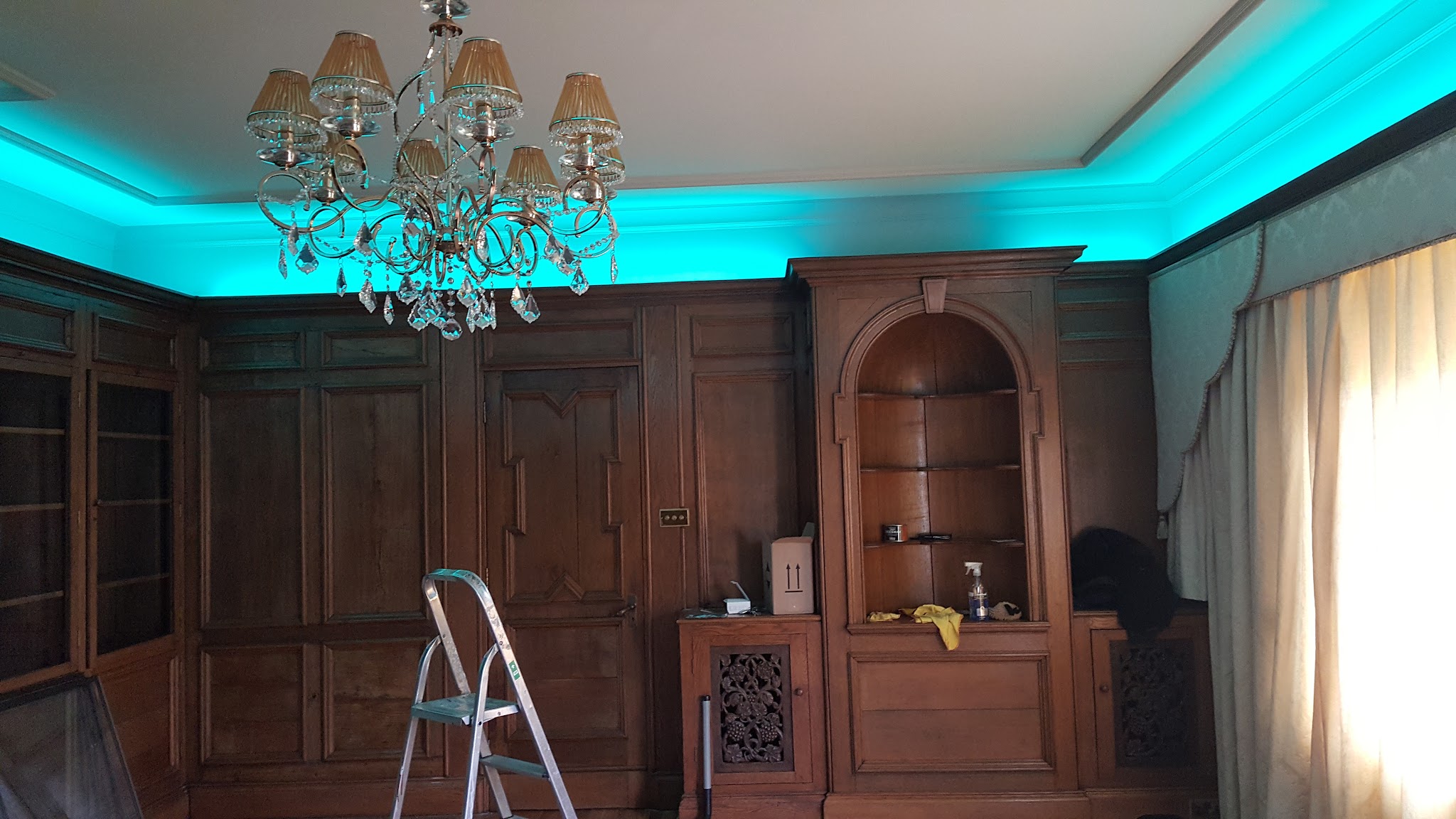 A panelled room lit with cyan cove lighting and a chandelier