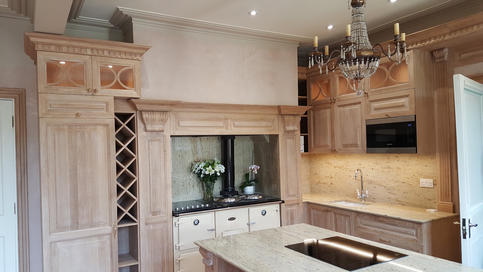 A fitted kitchen with a chandelier and lit worktops