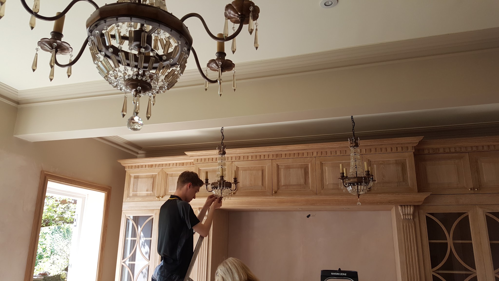 An electrician hanging a chandelier in a kitchen